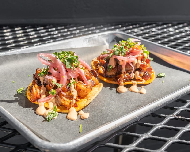 Two vibrant tostadas topped with meat, pickled red onions, cilantro, and creamy sauce on a tray.