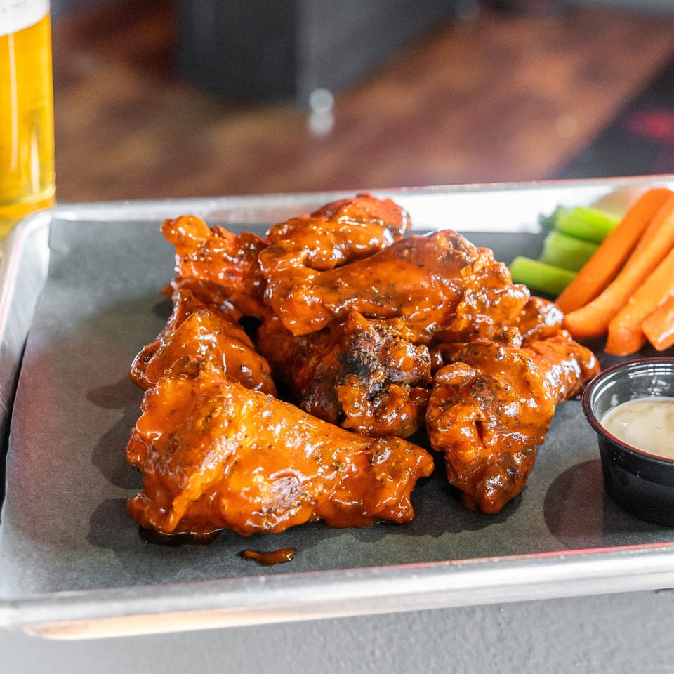 A tray of buffalo wings with celery, carrots, and dipping sauces, next to a glass of beer.