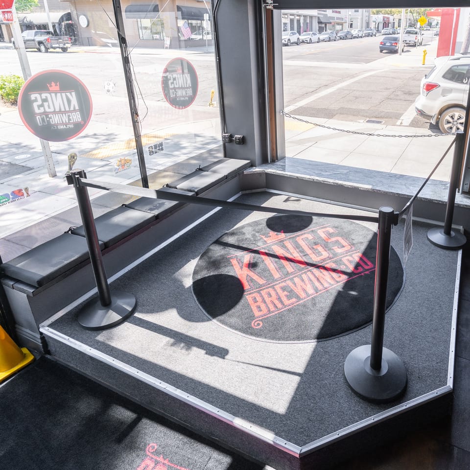 A roped-off entrance area with a Kings Brewing Co. logo mat and street view outside.