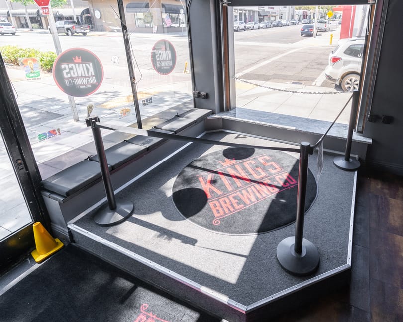 A roped-off entrance area with a Kings Brewing Co. logo mat and street view outside.