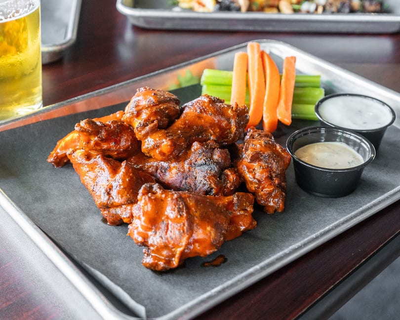 A tray of buffalo chicken wings with celery, carrots, and two dipping sauces, next to a beer.